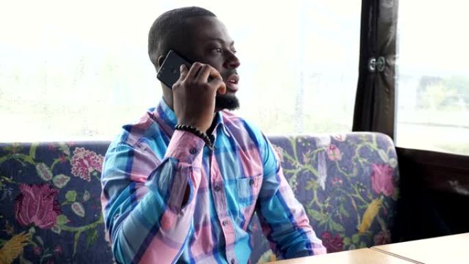 美国黑人男子打电话和聊天坐在咖啡馆里等待他的订单的智能手机。