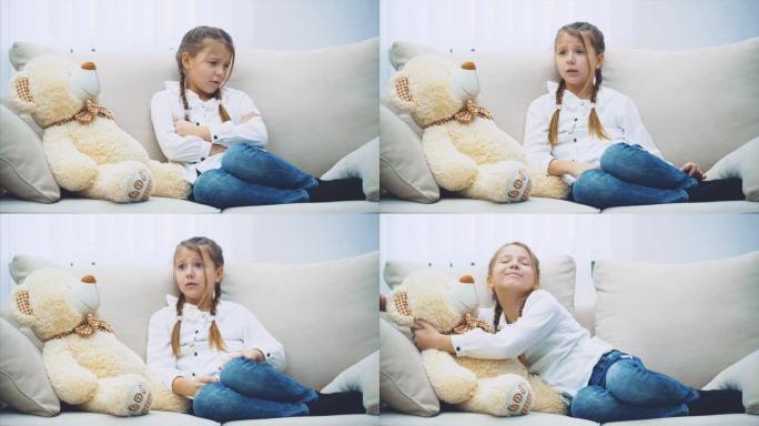 可爱的小女孩坐在沙发上，与她的泰迪熊交谈，deparparately解释，知道它不理解她，但拥抱着这