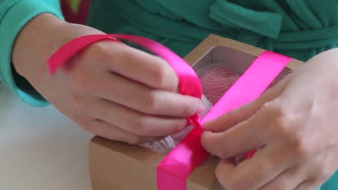一个女人正在包扎棉花糖礼品盒。不同颜色的棉花糖，通过盒子中的透明窗口可见。