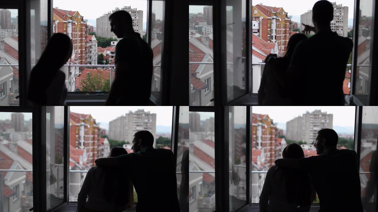 幸福的夫妇拥抱着，看着他们新公寓的窗户