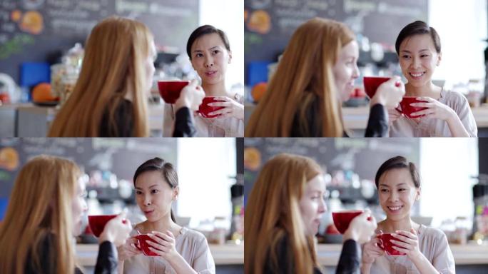 追踪两名年轻女子在咖啡馆喝茶或喝咖啡并聊天的正确镜头。亚洲女性向散焦的高加索朋友讲故事