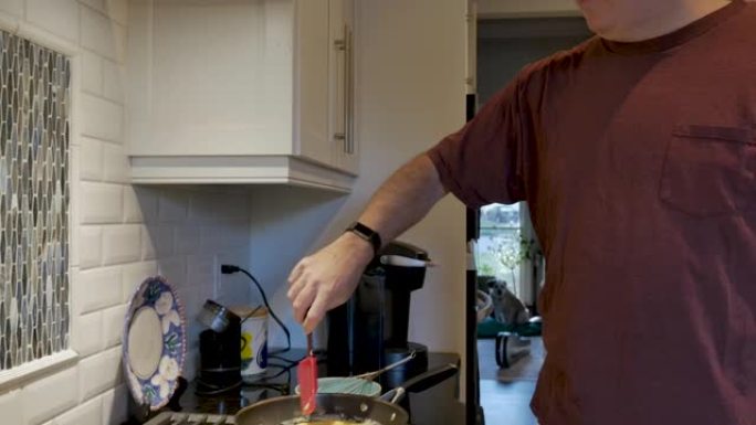 男子在厨房里用红色硅胶刮刀在煎锅里搅拌鸡蛋