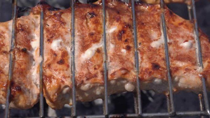 美味多汁的猪肉牛排在木炭烤架上的金属串上烹饪，并带有火烟