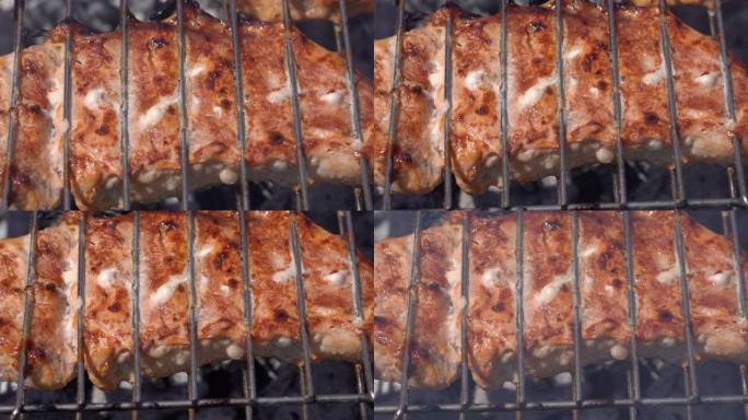 美味多汁的猪肉牛排在木炭烤架上的金属串上烹饪，并带有火烟