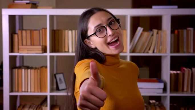 快乐而高兴的黑发女老师在图书馆示意竖起大拇指以示喜欢和尊重。