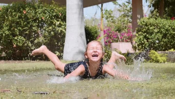 快乐的小女孩喜欢溅在公园草坪上的水坑里。