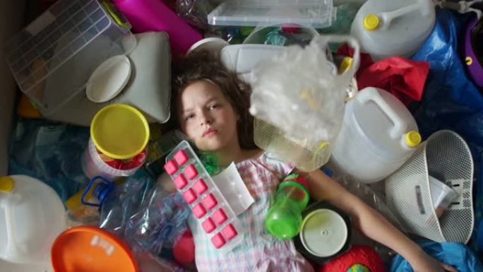 女学生躺在一堆塑料垃圾中，一个塑料袋落在女孩身上。地球的塑料污染，零废物运动