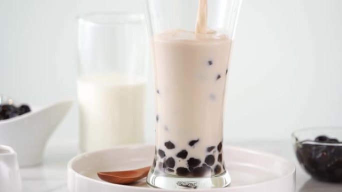慢动作-将奶茶倒入玻璃杯中，在明亮的大理石桌子和白色托盘上放美味的台湾木薯珍珠泡泡。4k视频拍摄。