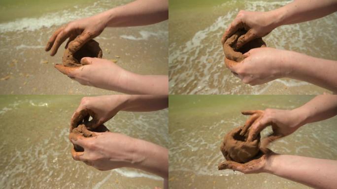 双手在沙滩上制作粘土的特写镜头，沙子和波浪作为背景，夏天和旅行概念。
