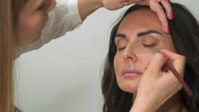 专业化妆师用刷子在女人脸上蒙上阴影