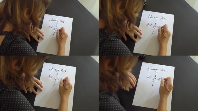一个年轻女子使用刻字技术在纸上写字的特写镜头。她写了梦想的大设定目标采取行动