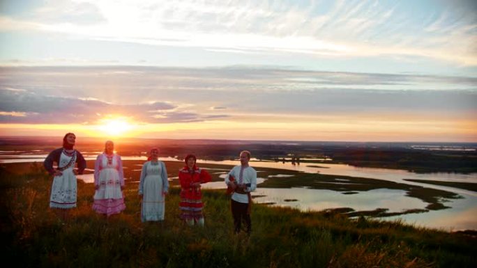 穿着俄罗斯传统服装的年轻人站在美丽的日落和歌唱的背景上