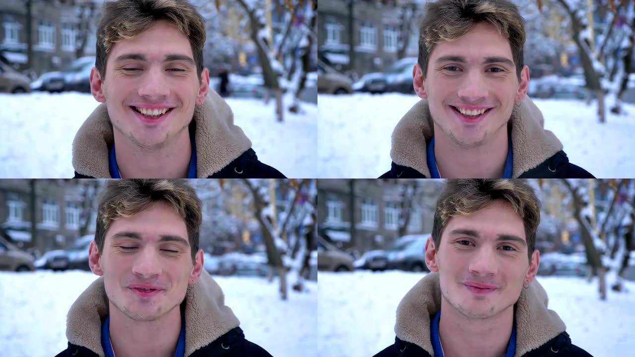 在下雪的冬日里，年轻迷人的白人男性看着相机，微笑着站在外面的特写肖像