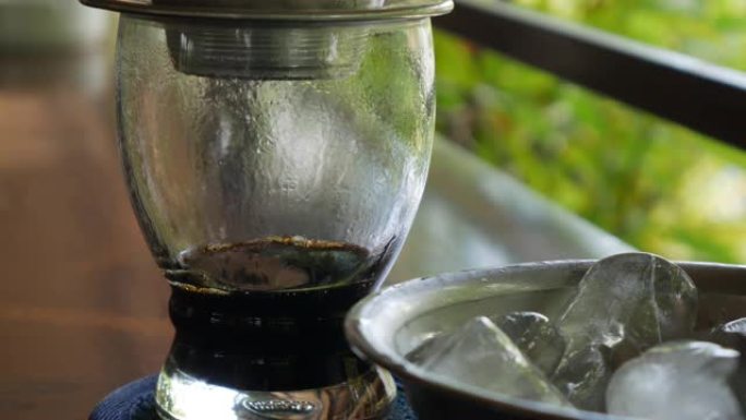 顾客在咖啡馆喝冰茶等待使用越南传统的phin过滤器酿造黑咖啡。咖啡在玻璃杯中慢慢滴落。Ca phe 
