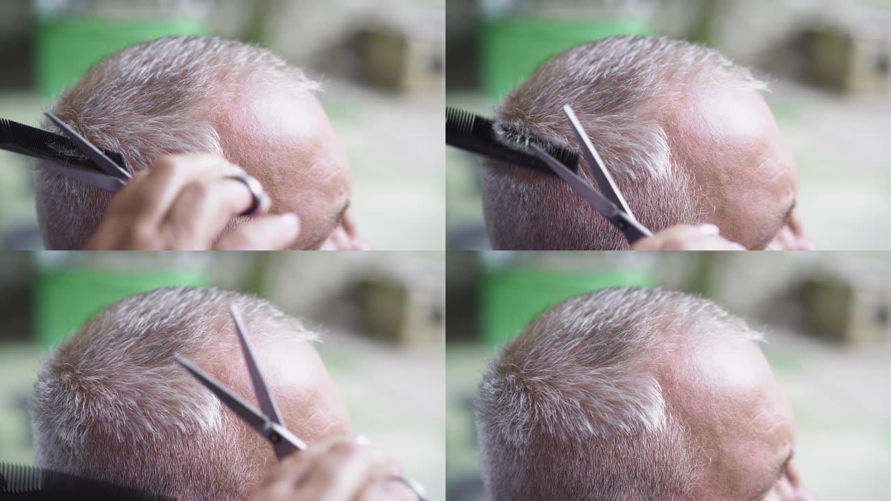 男人被理发师理发。女理发师用机器剪白发的男人。夏天在户外理发。特写
