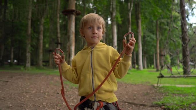 森林冒险公园里的小男孩展示了他的安全带。户外娱乐中心，为成人和儿童提供爬山活动，包括滑索和各种障碍物