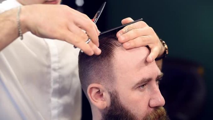 客户后面的理发师用手指、剪刀在前叉剪头发。大胡子男人理发的裁剪侧视图