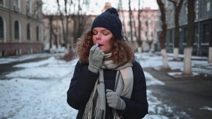 冬天，年轻女子站在城市的白雪皑皑的街道上涂口红。