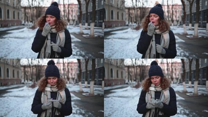 冬天，年轻女子站在城市的白雪皑皑的街道上涂口红。