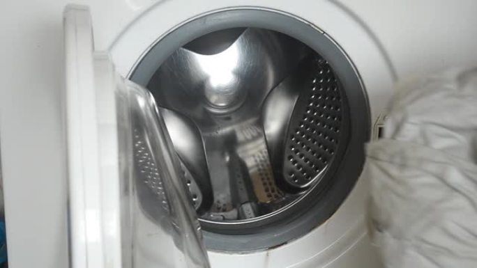 一个男人把浅色脏亚麻布放在洗衣机滚筒里。家庭作业。