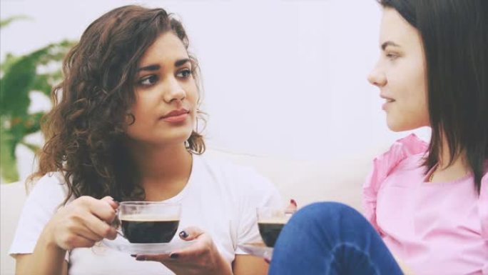 在温暖的家庭环境中，两个女孩朋友坐在沙发上聊天，喝着咖啡。