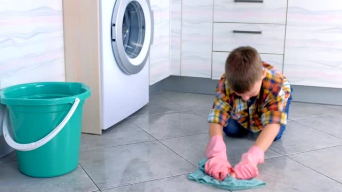 戴橡胶手套的疲倦男孩在厨房洗地板。