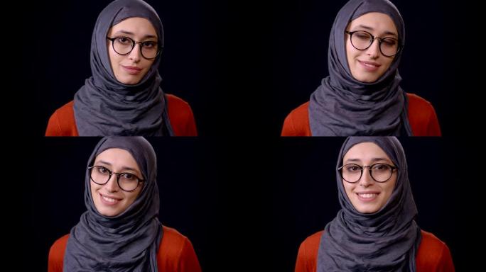 戴着头巾的年轻迷人穆斯林女性的特写镜头看着相机，微笑着，背景孤立在黑色上