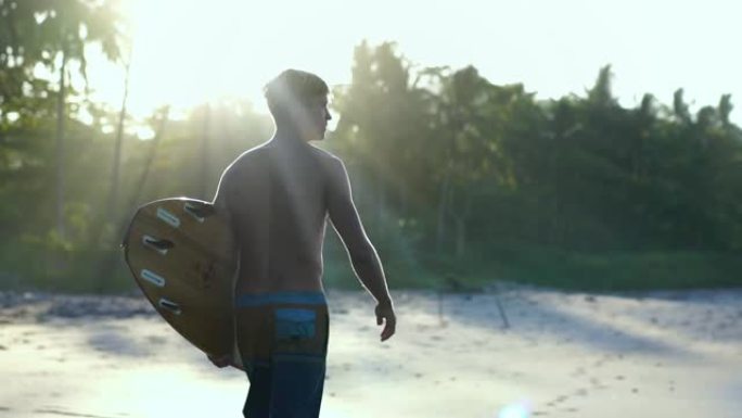 年轻迷人的冲浪者在日出时带着冲浪板走在海滩上，夏季冲浪冒险，自由精神的生活方式