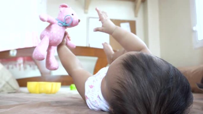 亚洲宝宝在床上拥抱她的粉红色熊娃娃。女婴喜欢她的熊娃娃朋友。