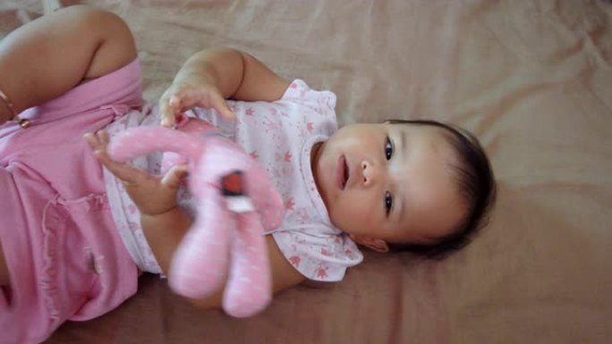 亚洲宝宝在床上拥抱她的粉红色熊娃娃。女婴喜欢她的熊娃娃朋友。