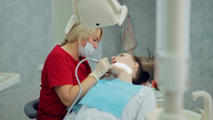 女牙医用硼机轻轻给病人钻一颗牙。用现代设备治疗牙科诊所的龋齿。