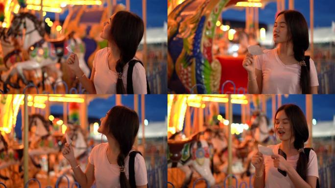美丽的亚洲女人寻找游乐园嘉年华玩旋转木马的票，人们生活方式亚洲旅游之夜游乐场4k分辨率。