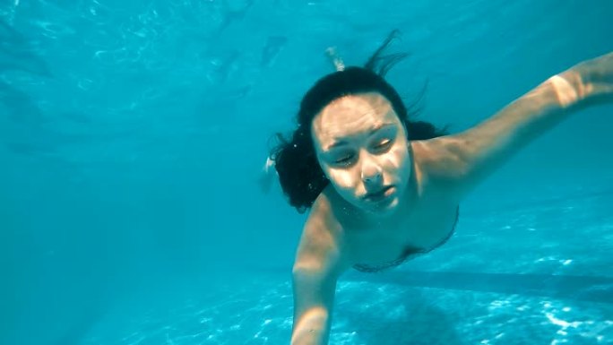十几岁的女孩在游泳池里惊慌失措地让鬼脸淹没在水下，慢动作