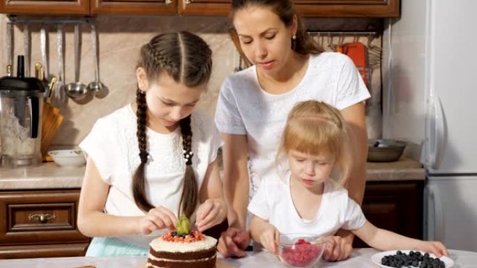 家庭，有两个小女儿的妈妈正在家里的厨房里一起用浆果装饰生日蛋糕。
