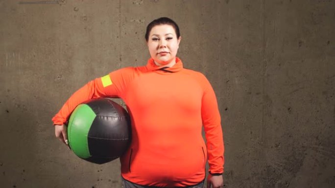 愉快的超重女人与运动球隔离在灰色背景