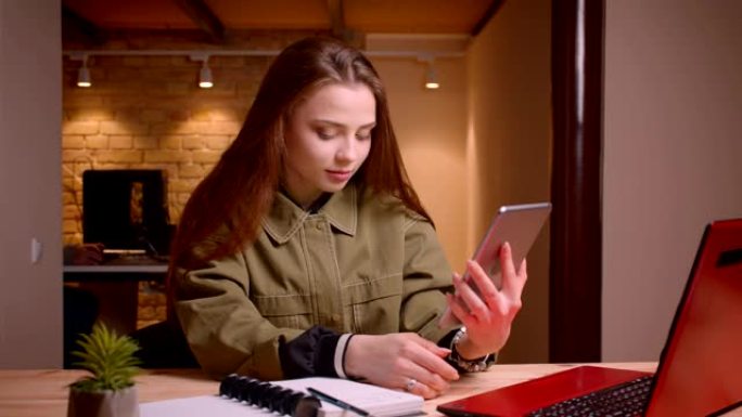 与平板电脑一起工作的年轻少女的肖像将其绿色色度屏幕显示在办公室的相机中。