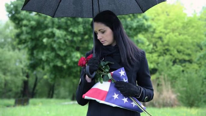 在公墓举着美国国旗的阵亡士兵的遗孀