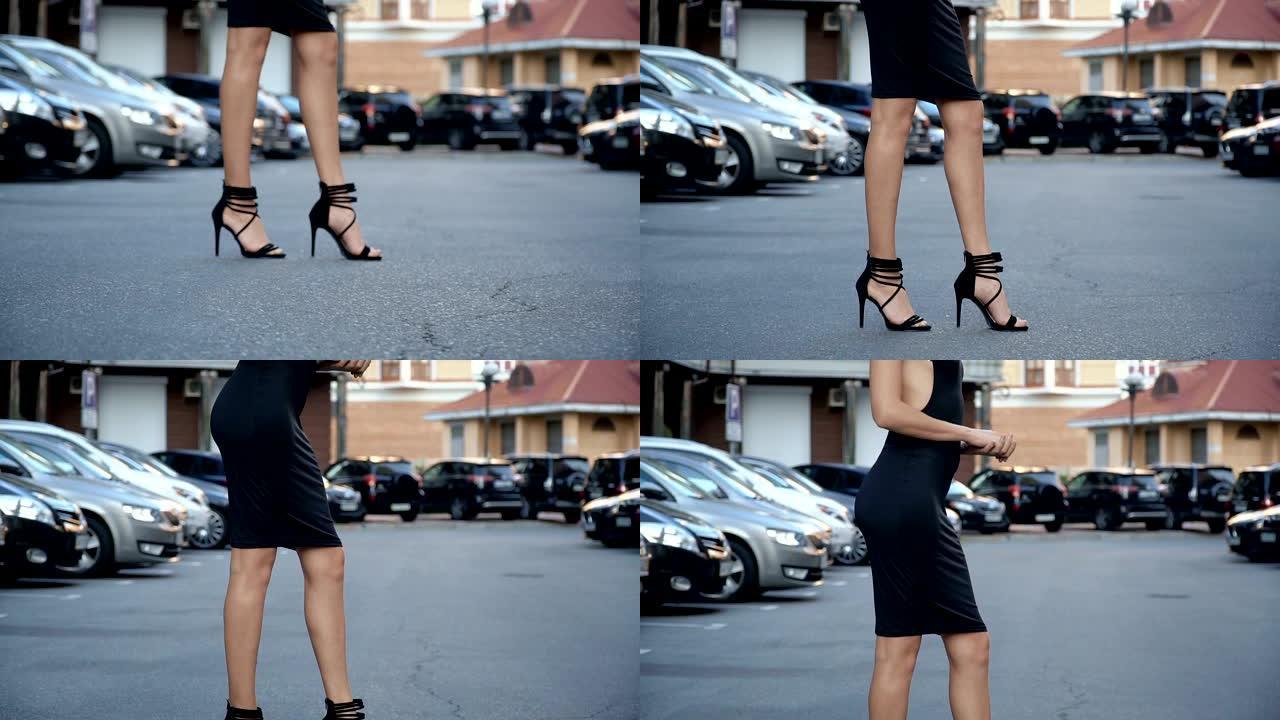 穿着时髦的黑色连衣裙的苗条女孩在停车场摆姿势。摄像机从底部到顶部的布线
