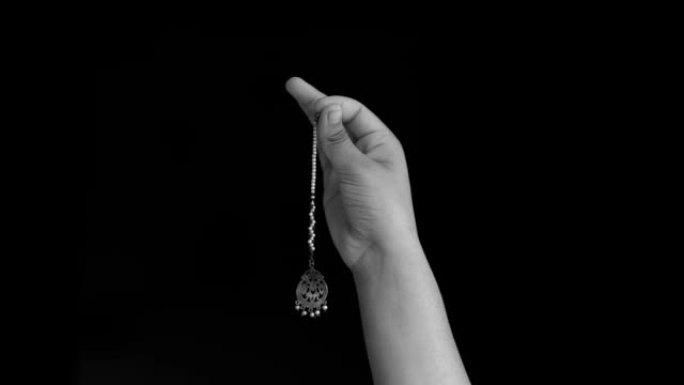 一只女性的手举起，在黑色背景上孤立地展示了maang tikka (女士在发际线上佩戴的印度珠宝)。
