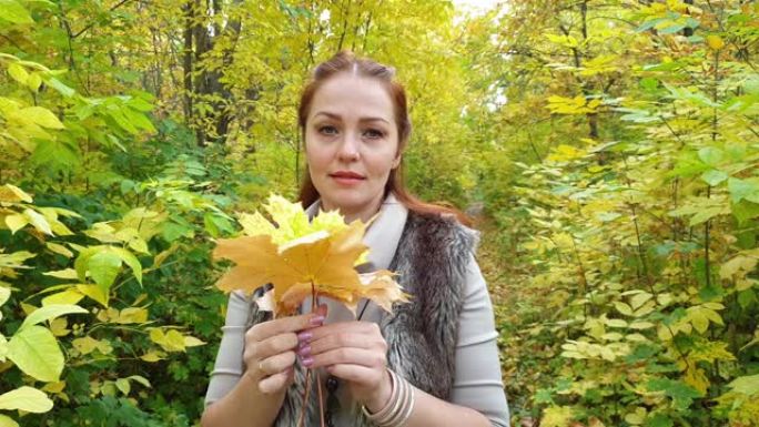 秋天公园里的迷人女人手里拿着黄色的叶子