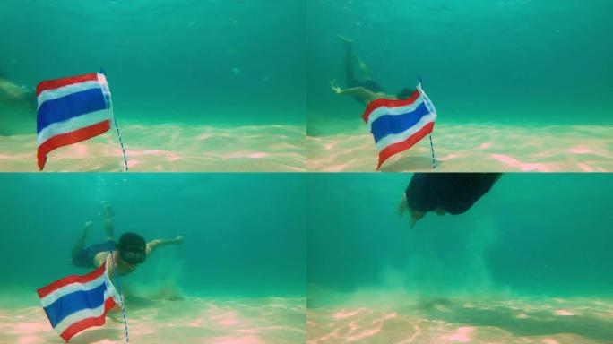 一名男子浮潜潜水并从海底拿走泰国国旗的慢动作镜头。被热带鱼包围的旗帜。泰国旅游概念。泰国的潜水和浮潜