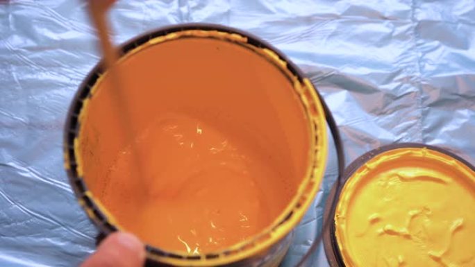 油漆工用棍子在罐中搅拌黄色墙漆。