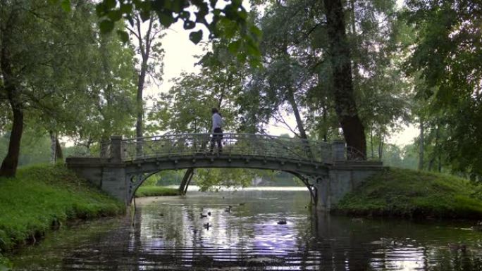 两个恋爱中的年轻人的侧视图穿过湖上方公园的一座小桥