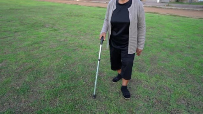 在草地上用手杖走路的高级女性腿的慢速运动