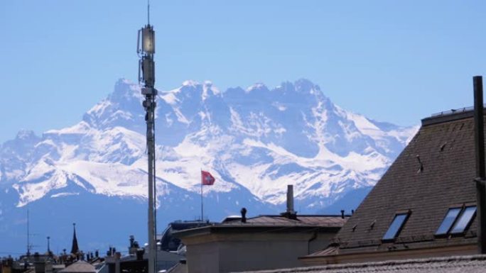 瑞士房屋屋顶上的景观和白雪皑皑阿尔卑斯山背景上的瑞士国旗