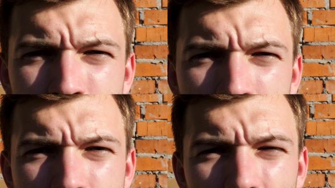 男人的棕色眼睛凝视着眼睛，并以自信的眼光斜视着相机。在砖墙背景上，被太阳照亮的男性面孔的肖像看着相机
