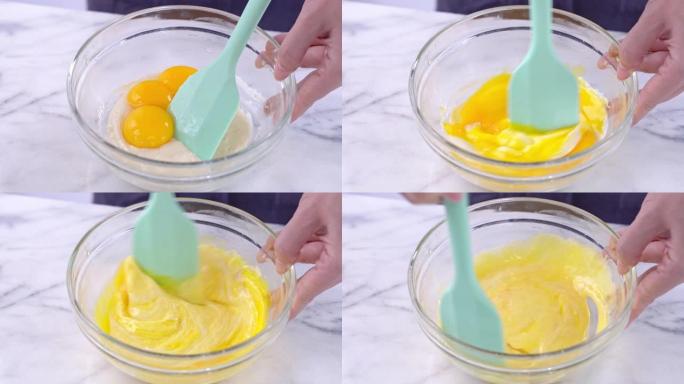 用绿色硅胶刮刀将蛋黄混合到雪纺蛋糕面糊中搅拌工具搅拌直至光滑，并在玻璃碗中充分混合，4k特写视图。