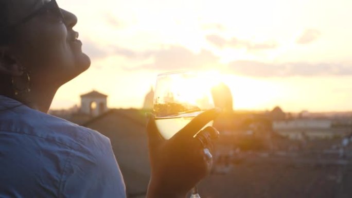 日落时，来自坎皮多利奥露台的罗马城市景观全景前，年轻女子旅游时尚白色连衣裙配一杯白葡萄酒。地标，意大