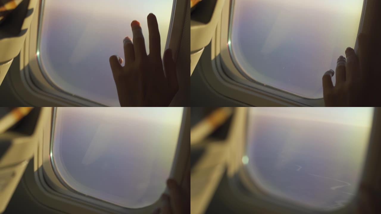 从飞机的窗户看。女人的手触摸舷窗。飞机在地面和云层上空高空飞行