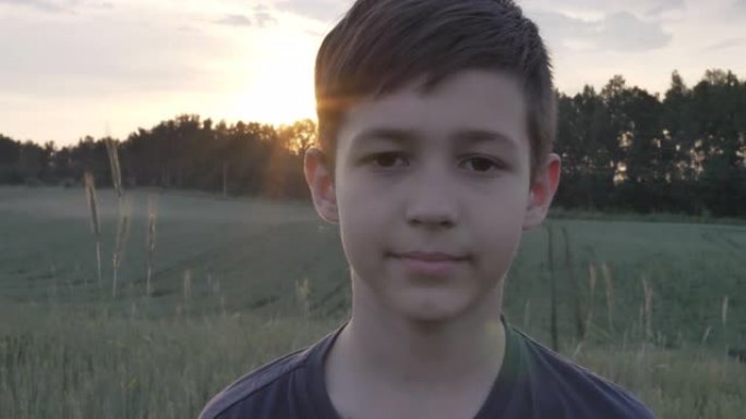 一个有趣的男孩在麦田里的肖像在日落时看着相机